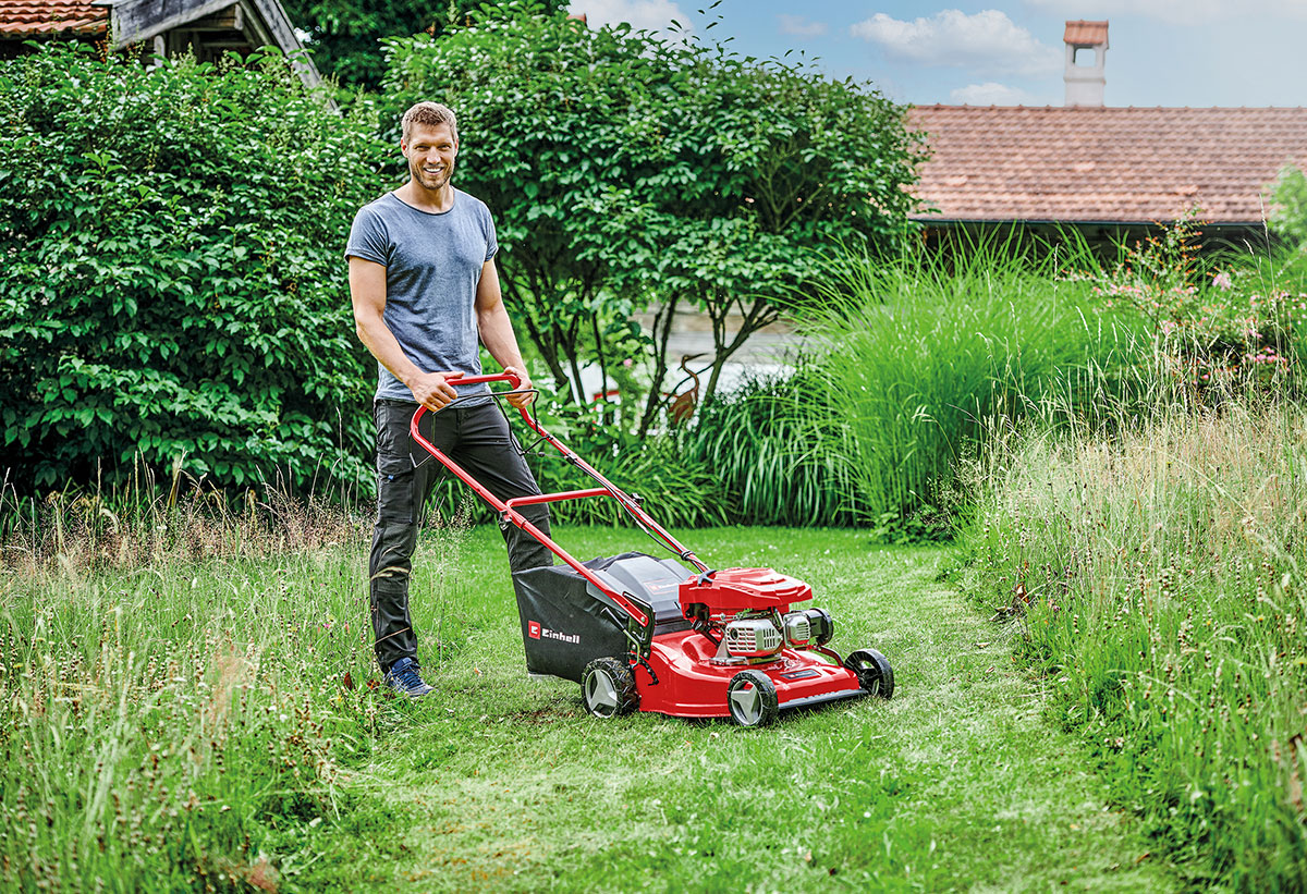 Άνδρας σε κήπο χρησιμοποιεί το Einhell GC-PM 46/3 για να κόψει γκαζόν, αναδεικνύοντας την ευκολία χειρισμού του.